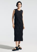 A person with short dark hair is wearing the TYPE-W 009-2, a sleeveless black textured dress with a relaxed fit by A-POC ABLE ISSEY MIYAKE, paired with black sandals, standing against a light background.