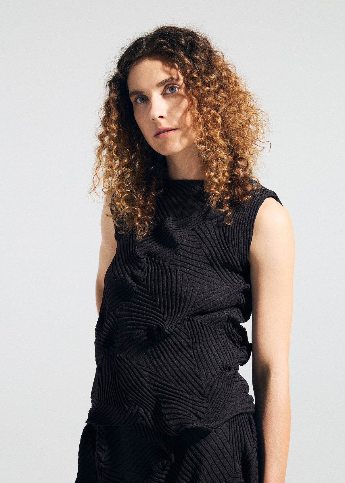A person with curly brown hair wears the sleeveless, textured TYPE-P 003-2 dress by A-POC ABLE ISSEY MIYAKE, crafted with the Baked Stretch technique, standing against a plain background—ideal for versatile everyday wear. view 6 of 10