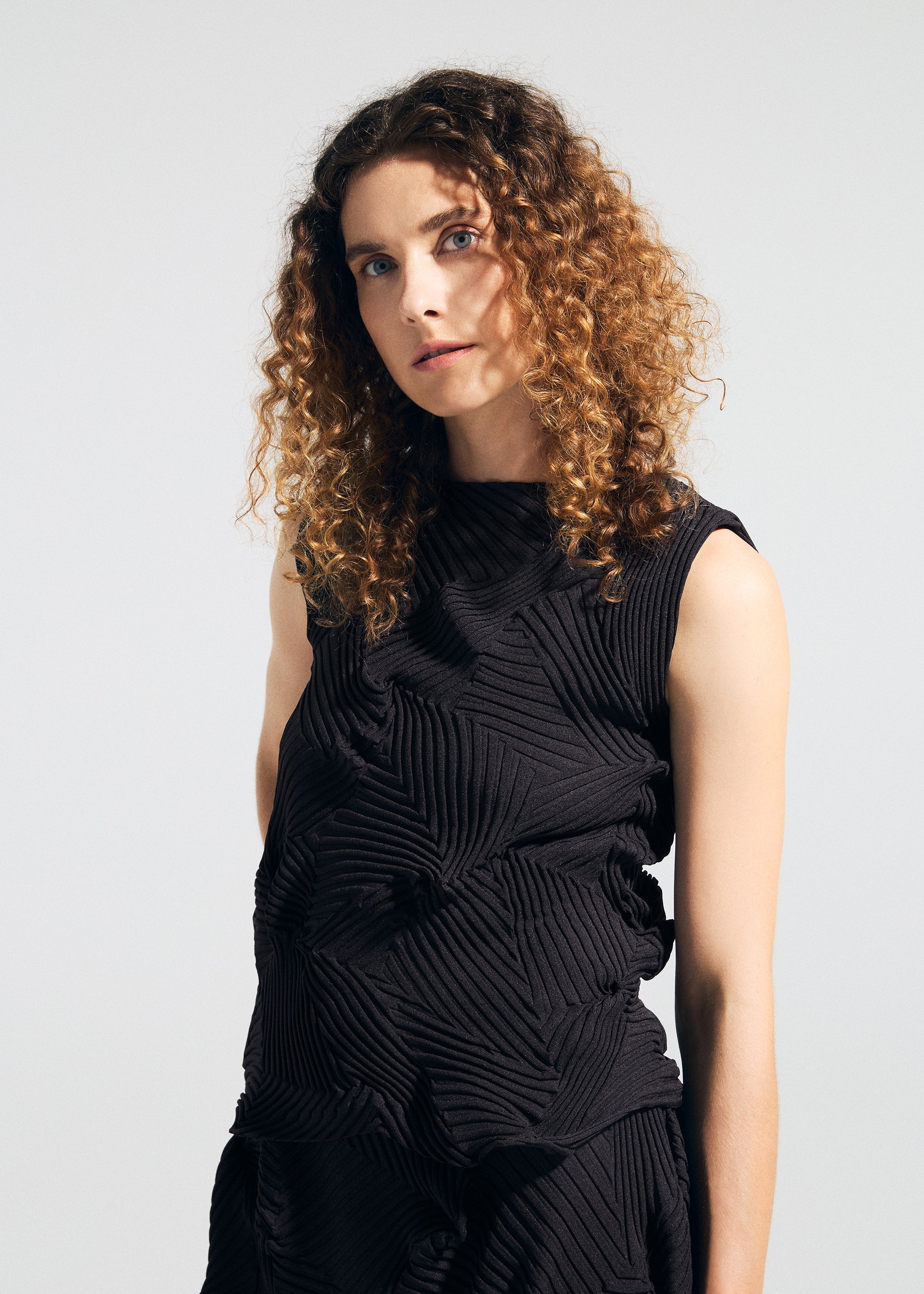 Zoomed view A person with curly brown hair wears the sleeveless, textured TYPE-P 003-2 dress by A-POC ABLE ISSEY MIYAKE, crafted with the Baked Stretch technique, standing against a plain background—ideal for versatile everyday wear.