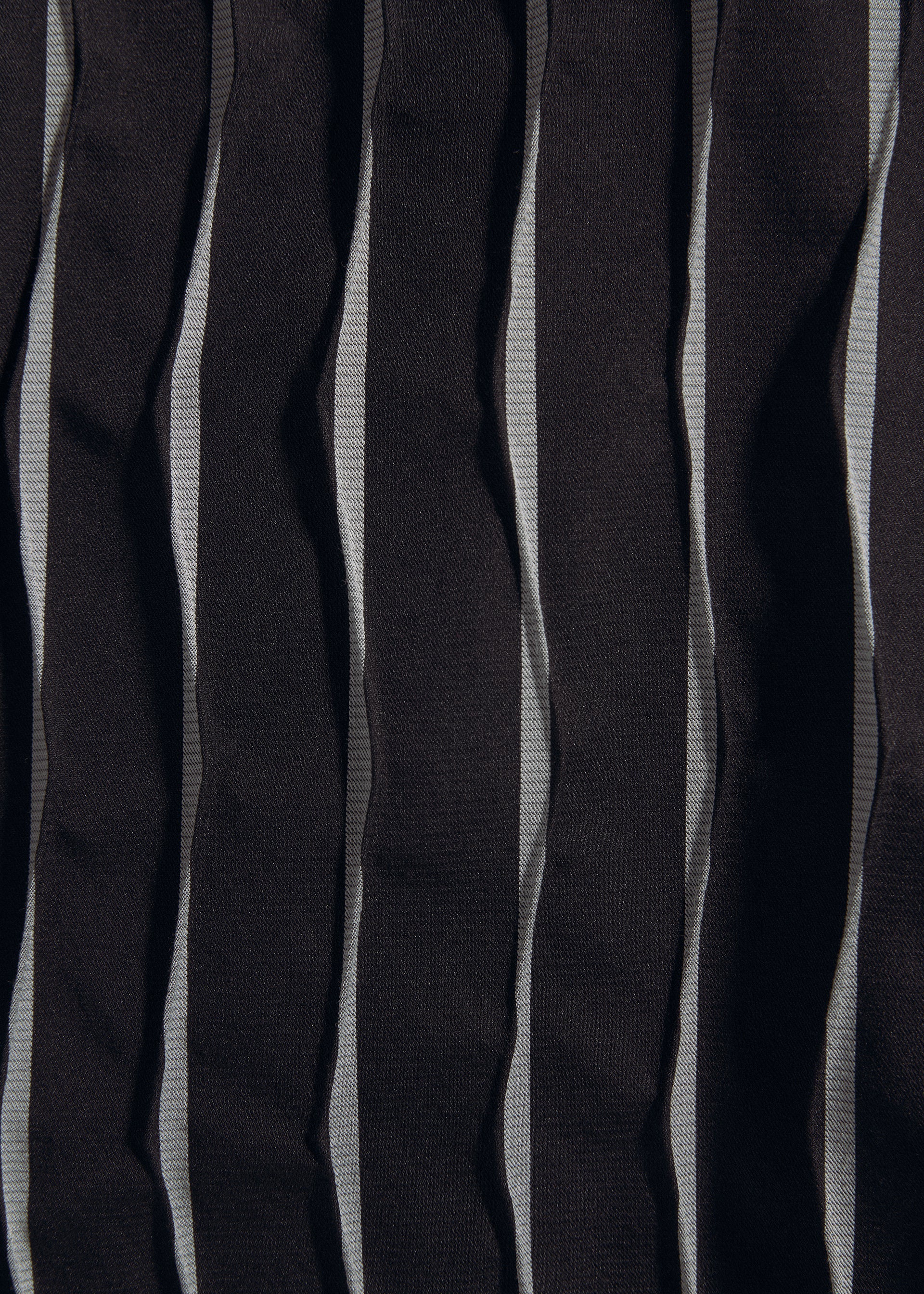Zoomed view A close-up of TYPE-W 011 by A-POC ABLE ISSEY MIYAKE: vertically striped black and gray fabric with zigzag pleats, featuring a wrinkled, textured surface inspired by Steam Stretch techniques.
