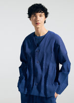 A person with short, curly hair wears the TYPE-W 009-2 cardigan by A-POC ABLE ISSEY MIYAKE—a textured, deep blue piece featuring a relaxed fit and subtle geometric patterns—while standing against a light grey background.
