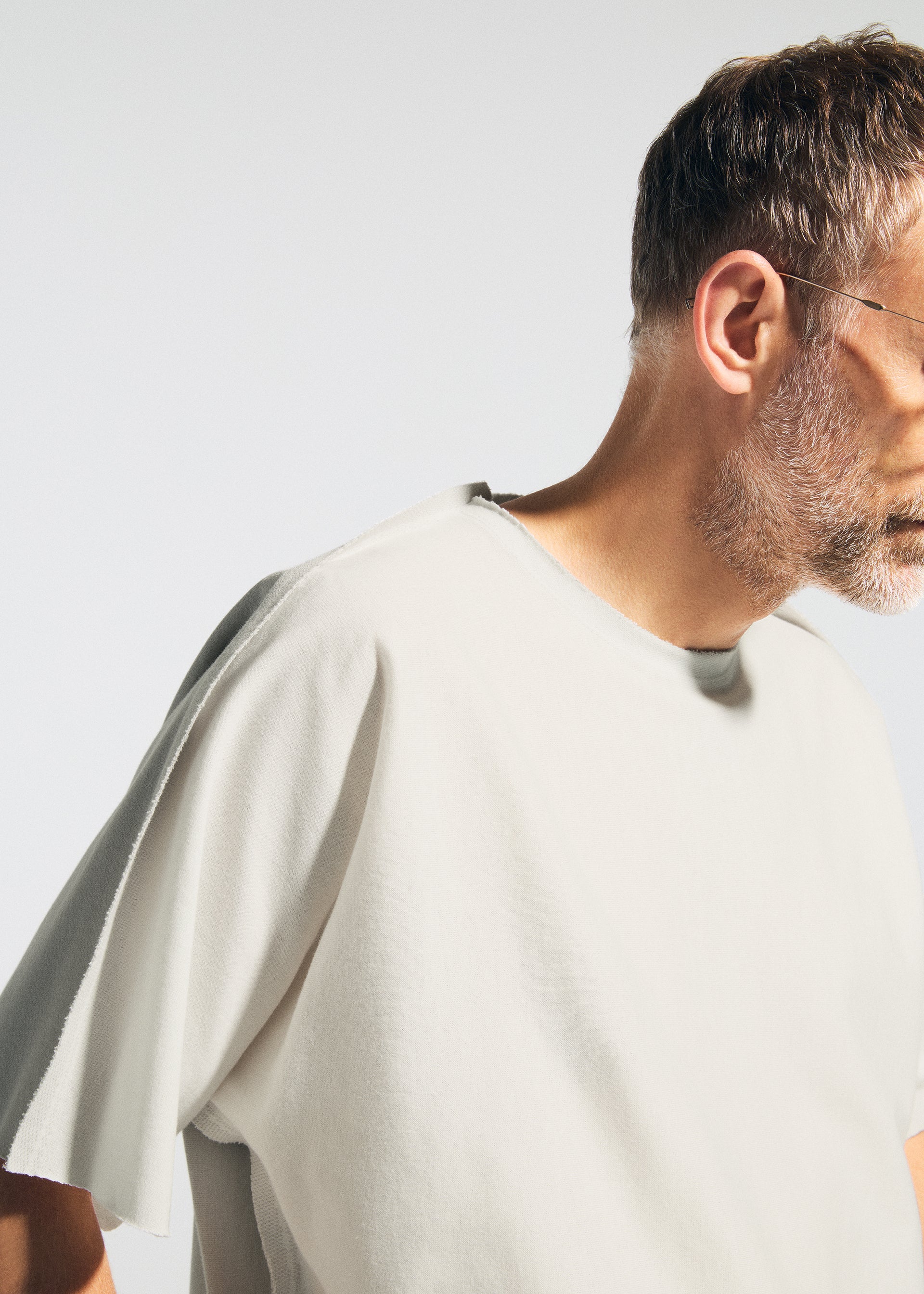 Zoomed view A man with short hair, a beard, and glasses wears the TYPE-J 001 two-tone knit oversized t-shirt by A-POC ABLE ISSEY MIYAKE, shown from the side against a light background with his face partially out of frame.