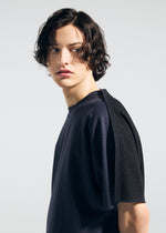 A person with wavy, chin-length dark hair wears the TYPE-J 001 loose, short-sleeved top by A-POC ABLE ISSEY MIYAKE, looking to the side against a plain light background.