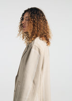 A person with shoulder-length curly hair models the TYPE-K 008 textured knit jacket by A-POC ABLE ISSEY MIYAKE in light beige, standing in profile against a plain white background.