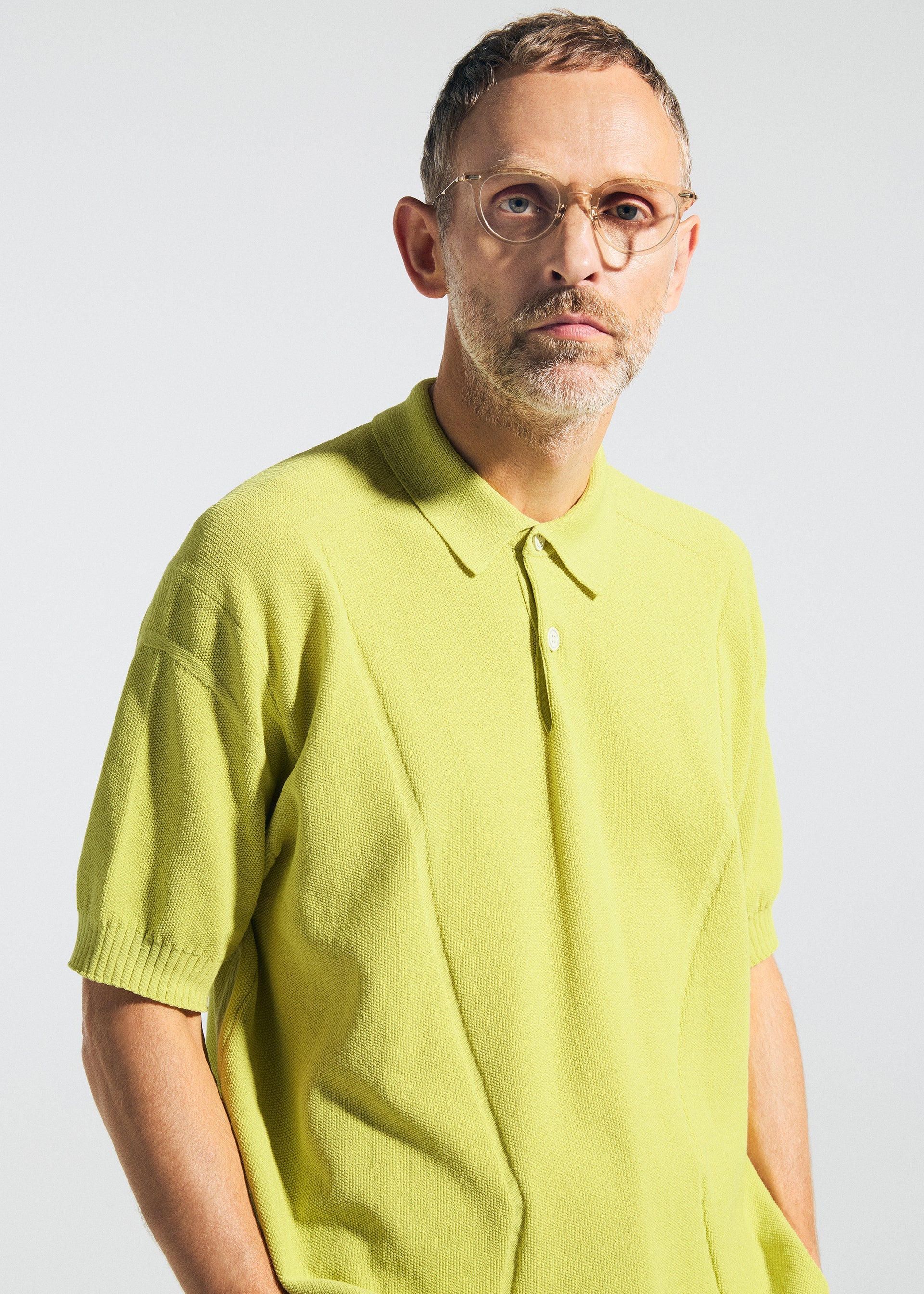 Zoomed view A man with short hair, a trimmed beard, and glasses wears the TYPE-K 003-2 light yellow-green knit polo shirt by A-POC ABLE ISSEY MIYAKE, standing against a plain background and looking directly at the camera with a neutral expression.