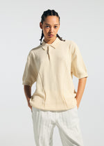 Wearing the TYPE-K 003-2 cream short-sleeved collared shirt by A-POC ABLE ISSEY MIYAKE and white pinstriped pants, a person with braided hair stands against a light background with hands in pockets.