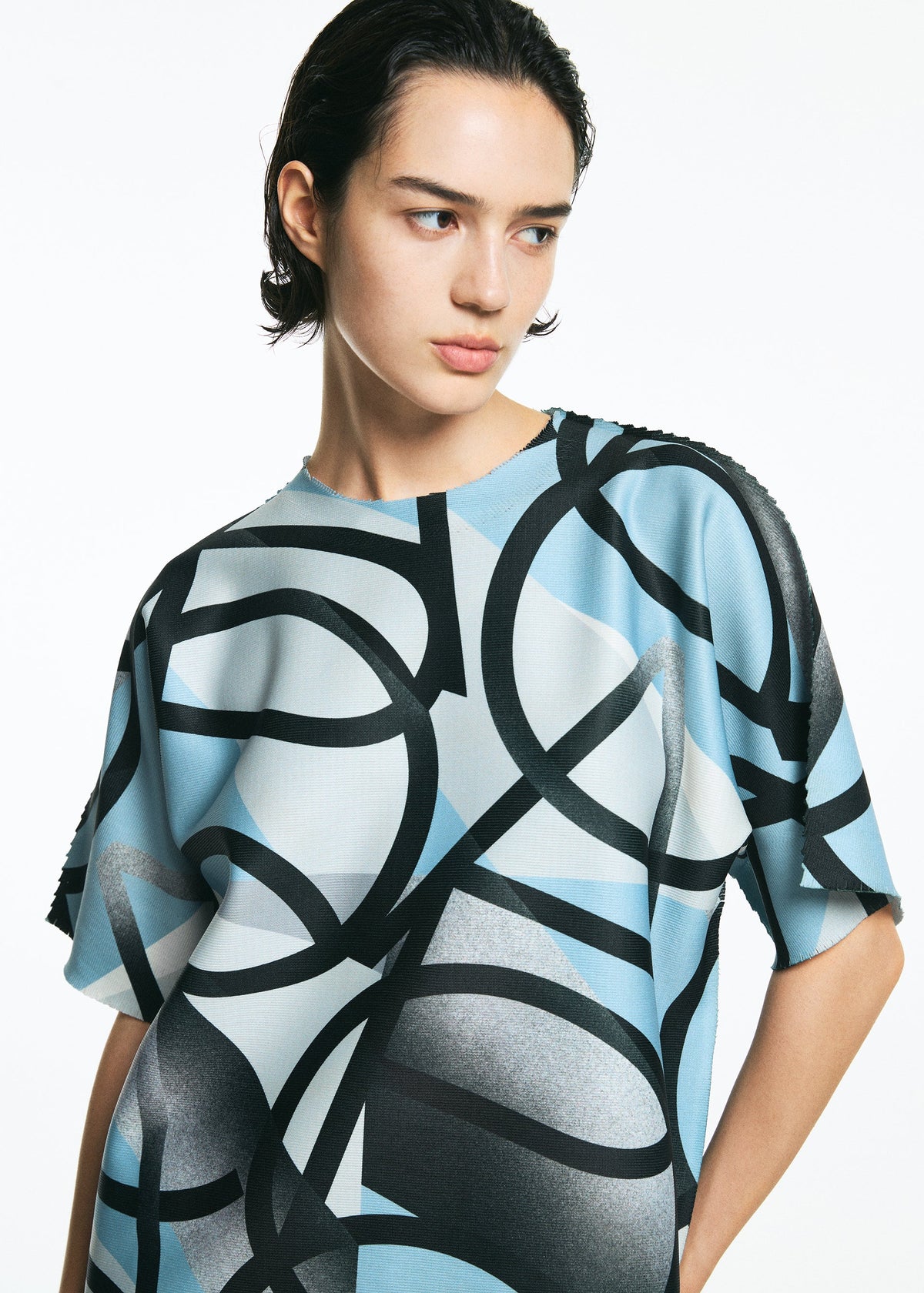 A person with short dark hair wears a loose-fitting, blue and white TYPE-XV SOAR NY project 002 shirt by A-POC ABLE ISSEY MIYAKE, featuring bold black abstract patterns, while looking slightly to the side against a plain white background. view 7 of 10