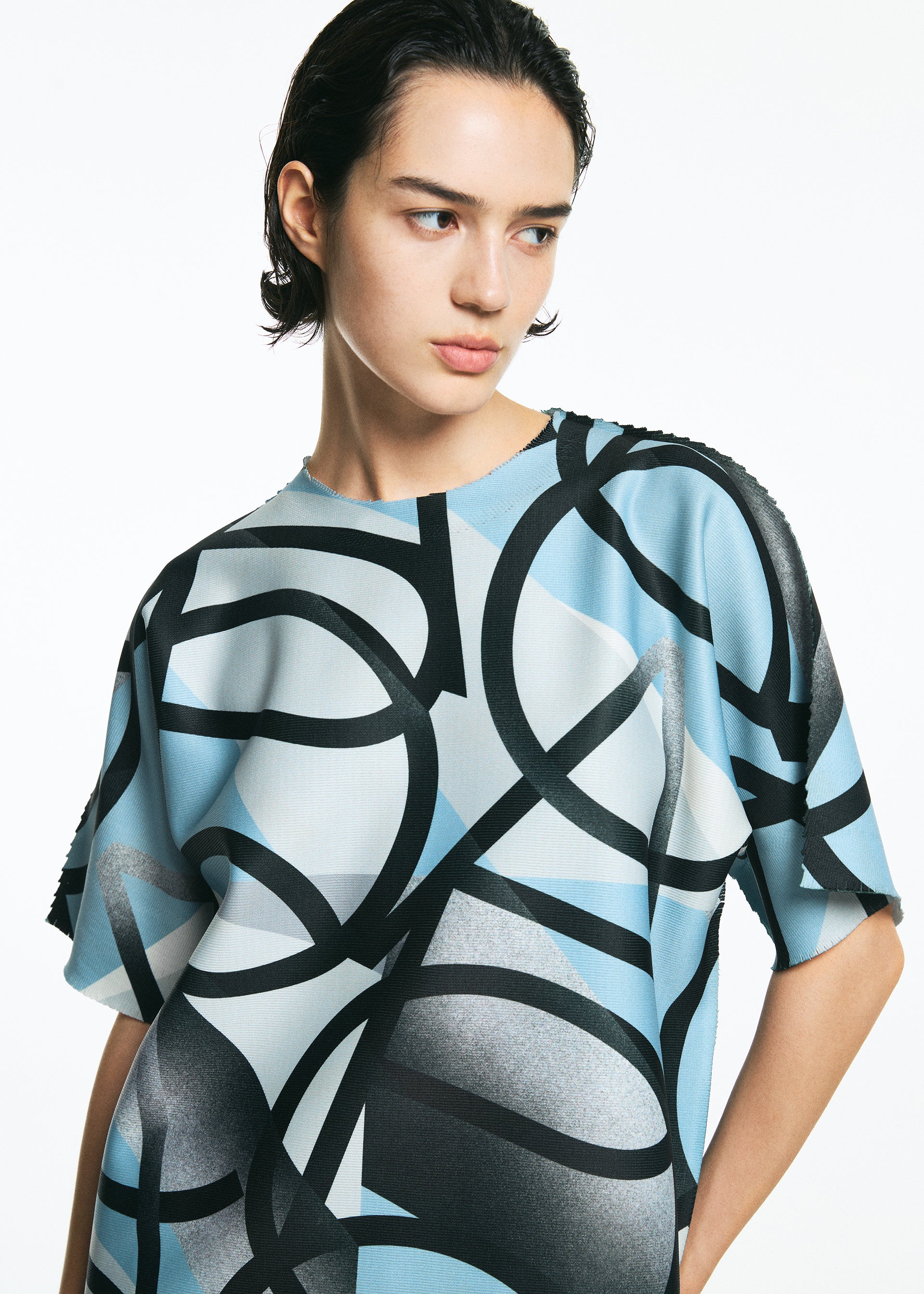 Zoomed view A person with short dark hair wears a loose-fitting, blue and white TYPE-XV SOAR NY project 002 shirt by A-POC ABLE ISSEY MIYAKE, featuring bold black abstract patterns, while looking slightly to the side against a plain white background.