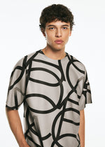 A young man with curly hair wears the TYPE-XV SOAR NY project 002 T-shirt by A-POC ABLE ISSEY MIYAKE, which features a bold black abstract pattern, standing against a plain white background.