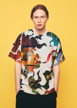 A person with red hair stands against a yellow background, wearing the TYPE-XII Tomokazu Matsuyama project 004 shirt from A-POC ABLE ISSEY MIYAKE, featuring a colorful, abstract pattern inspired by contemporary art collaborations. With hands in pockets, they look directly at the camera.