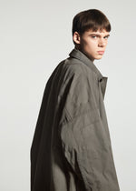 A young person with short brown hair wears the oversized, wrinkle-resistant TYPE-U 001-1 coat from A-POC ABLE ISSEY MIYAKE, glancing over their shoulder against a plain light background.