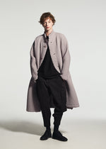 A person wears the TYPE-O 024 long coat by A-POC ABLE ISSEY MIYAKE in textured light gray, styled over a black top and pants with black shoes, standing against a plain white background.