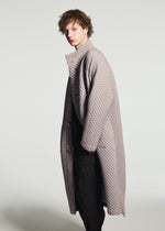 Person with short curly hair wearing the TYPE-O 024 long textured light gray quilted coat by A-POC ABLE ISSEY MIYAKE and black pants, standing sideways against a plain light background.