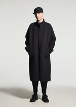 A person stands against a plain background wearing the TYPE-O 024 coat by A-POC ABLE ISSEY MIYAKE, styled with black pants, black lace-up shoes, and a black cap. Their hands are in the coat pockets.
