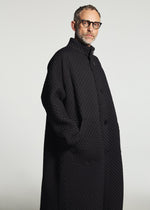 A man with short hair, a beard, and glasses wears the TYPE-O 024 coat by A-POC ABLE ISSEY MIYAKE. He stands with one hand in his pocket, looking to the side against a plain light background.