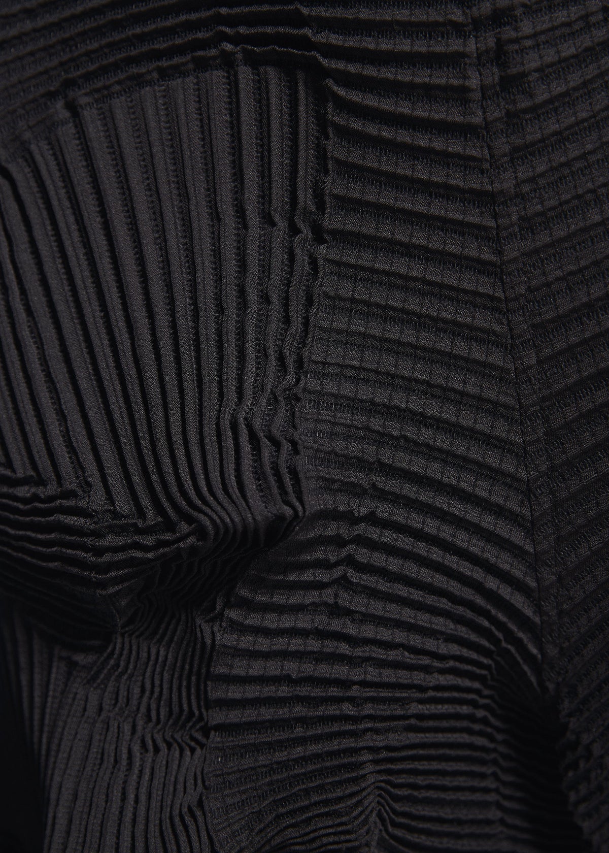 Close-up of black pleated fabric with textured, wavy ridges and geometric folds, showcasing varying depths and shadows. Crafted from recycled polyester, this unique textile is featured in the TYPE-O 003 BK pants by A-POC ABLE ISSEY MIYAKE. view 7 of 7