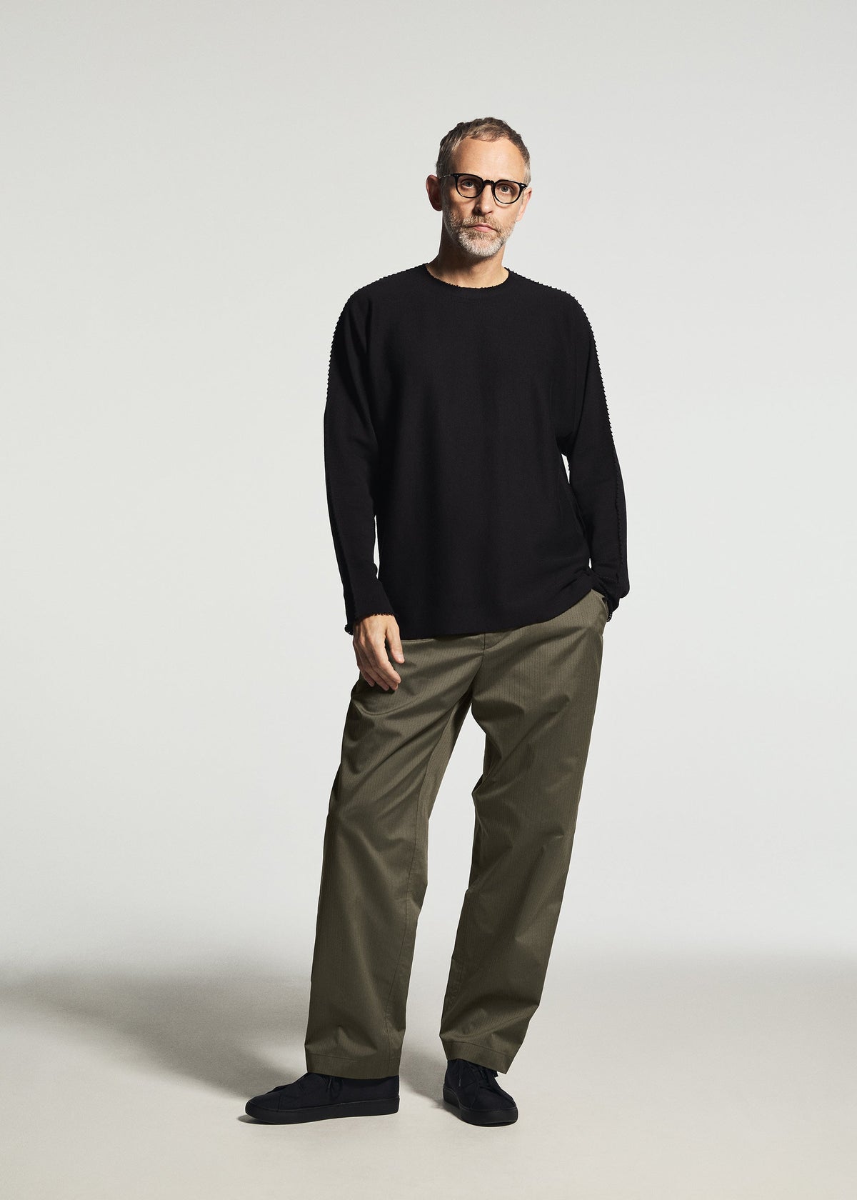 A man wearing TYPE-S 003 by A-POC ABLE ISSEY MIYAKE—olive green, lightweight, stretchy straight pants—pairs them with glasses and a black long-sleeve shirt against a plain light background. view 4 of 5