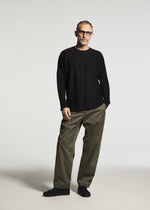 A man wearing TYPE-S 003 by A-POC ABLE ISSEY MIYAKE—olive green, lightweight, stretchy straight pants—pairs them with glasses and a black long-sleeve shirt against a plain light background.