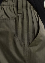 Close-up of TYPE-S 003 by A-POC ABLE ISSEY MIYAKE: olive green straight pants with elastic waistband, side pocket, subtle vertical pinstripes, and gathered fabric in lightweight stretch material.