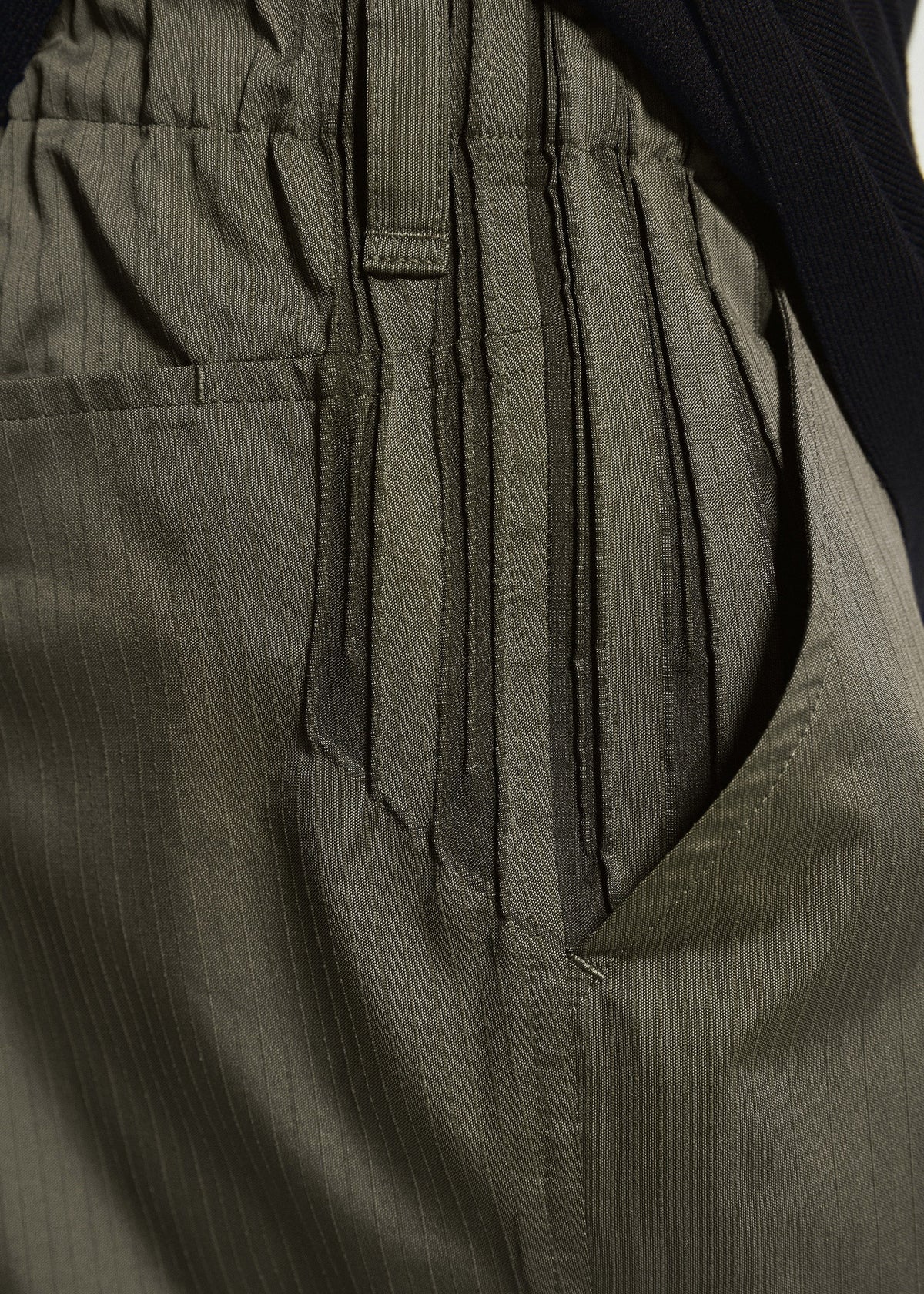 Zoomed view Close-up of TYPE-S 003 by A-POC ABLE ISSEY MIYAKE: olive green straight pants with elastic waistband, side pocket, subtle vertical pinstripes, and gathered fabric in lightweight stretch material.