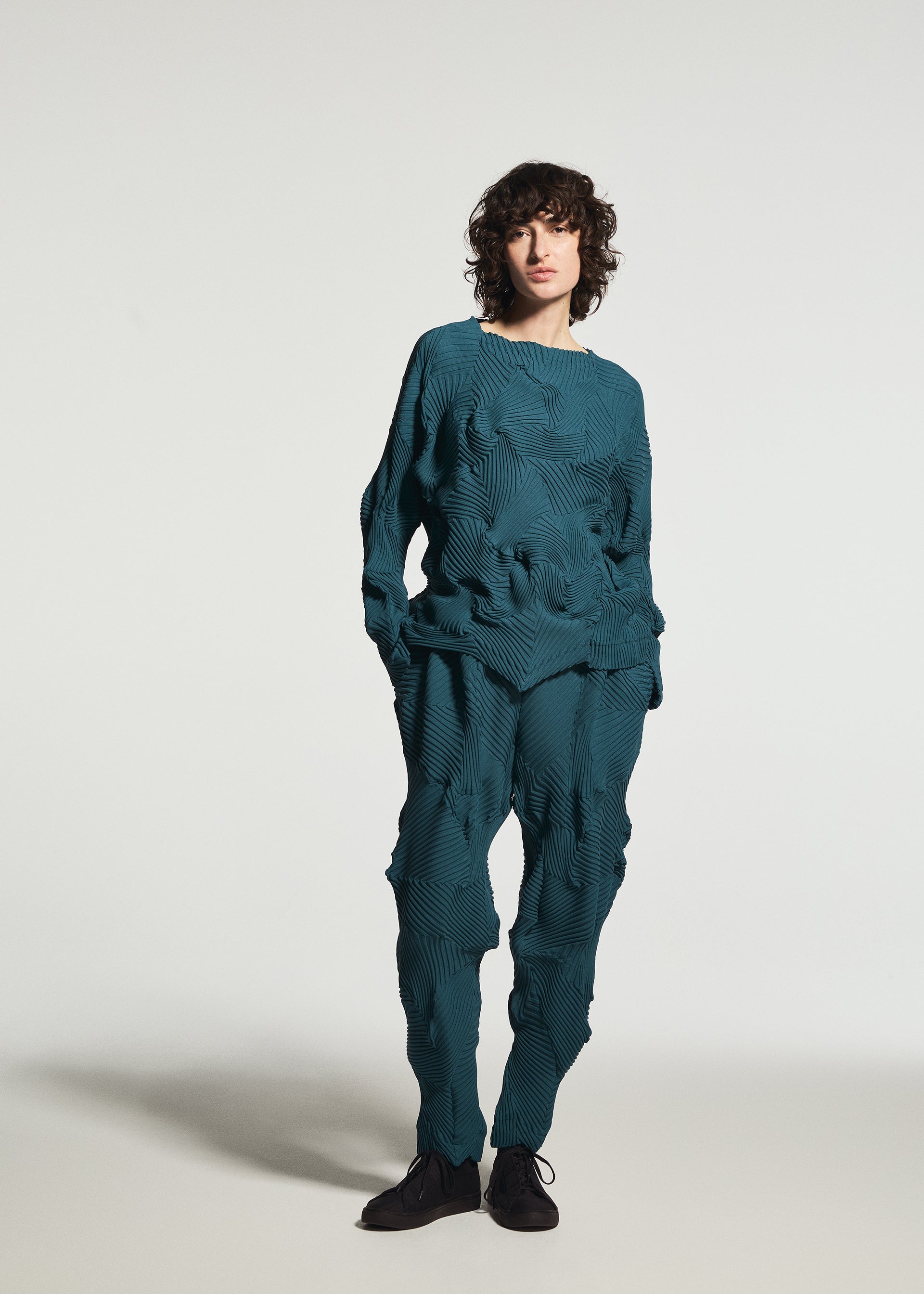 Zoomed view A person is wearing the TYPE-P 003-1 set by A-POC ABLE ISSEY MIYAKE, featuring a textured, teal long-sleeved top and matching pants with a wavy 3D pattern, standing against a plain white background.