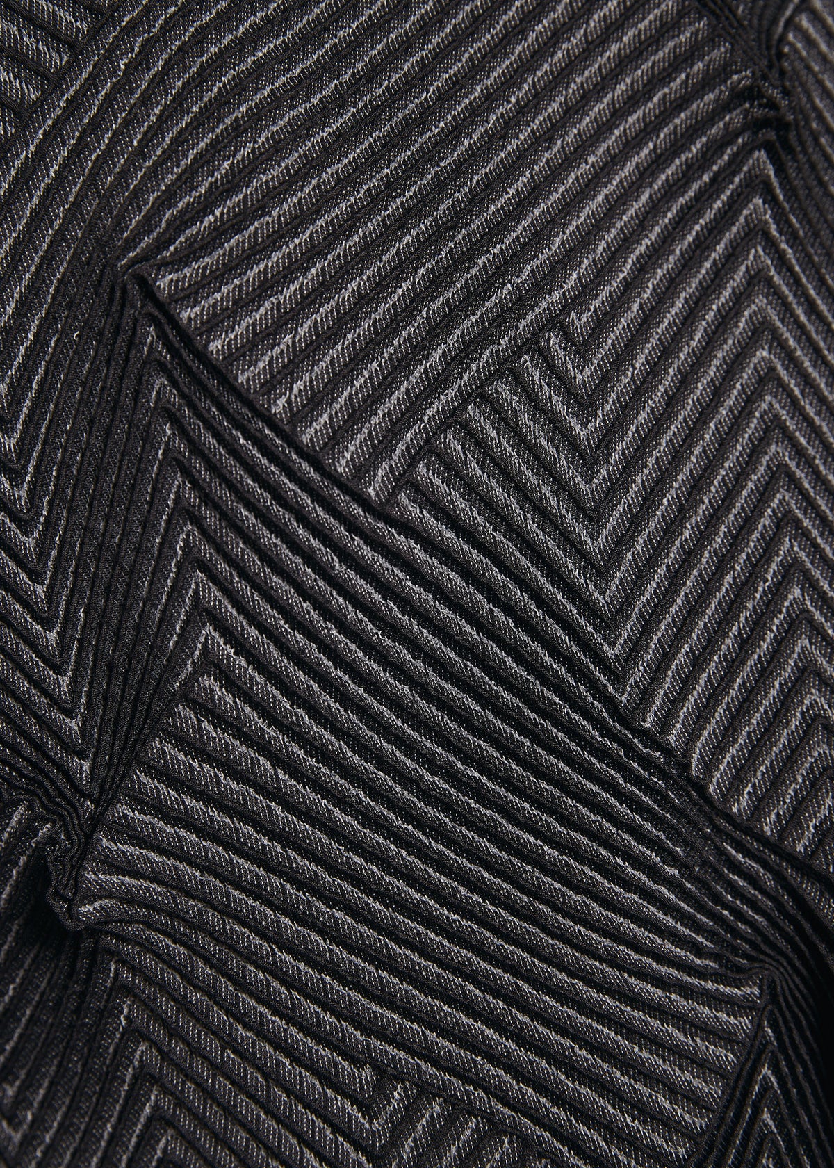 Close-up of TYPE-O 010-1 by A-POC ABLE ISSEY MIYAKE: black recycled polyester fabric with a chevron pattern of diagonal ribbed lines, creating a layered, three-dimensional effect. view 9 of 9