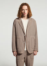 A person with shoulder-length curly red hair wears the TYPE-K 012 by A-POC ABLE ISSEY MIYAKE, a beige sashiko style suit jacket over a white shirt, standing against a plain white background.