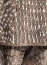 Close-up of TYPE-K 012 by A-POC ABLE ISSEY MIYAKE: textured brown and white sashiko-style fabric with a hemmed edge and small woven-like dots.