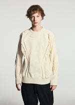 Wearing TYPE-K 001 from A-POC ABLE ISSEY MIYAKE, a person with short, curly hair stands against a plain light background. The cream-colored knit top showcases pleated details and black pants. Crafted from stretchy polyester using the innovative Steam Stretch technique, TYPE-K 001 offers both comfort and style.