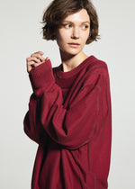A person with short brown hair wears the TYPE-K 010 by A-POC ABLE ISSEY MIYAKE, gazing sideways with hands together near their face against a plain light background.