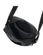 Top view of an open BAO BAO ISSEY MIYAKE VOYAGER crossbody travel bag with geometric patterns, showing the spacious main compartment and small inner pocket, both empty. This vertical shoulder bag features a black strap, zipper closure, and ample room for essentials such as a water bottle.