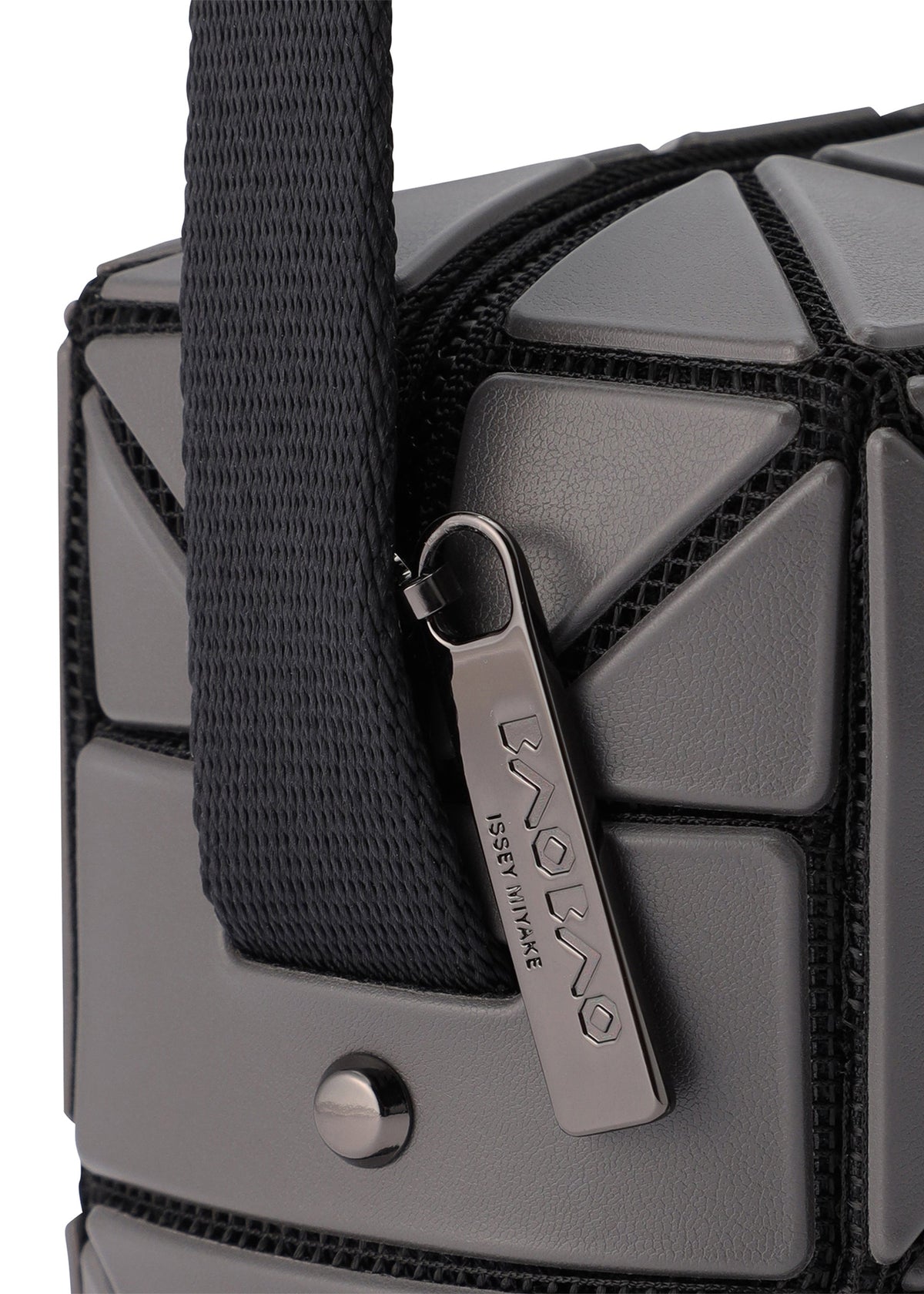 Close-up of the CUBOID shoulder bag by BAO BAO ISSEY MIYAKE, featuring a gray geometric pattern, black adjustable strap, silver engraved zipper pull, and metal snap button on its minimalist design. view 3 of 6