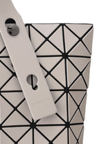 Close-up of the BAO BAO ISSEY MIYAKE PRISM MATTE-2 tote bag, featuring beige triangular panels with black outlines, fabric grain texture, a wide strap with two round black buttons, keyhole cutout, and visible branding. Fits A4 documents.