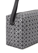 A close-up of the BAO BAO ISSEY MIYAKE SADDLE BAG REFLECTOR, featuring a gray geometric-patterned surface with black triangular lines and a thick black strap attached at the top corner.