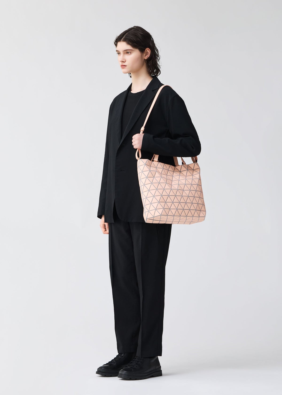 A person in a black suit and shoes stands against a plain background, carrying the chic BAO BAO ISSEY MIYAKE CRYSTAL MATTE handbag with leather straps—ideal for holding A4-size documents. view 6 of 6