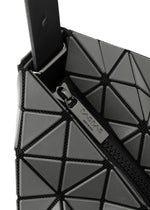 Close-up of the BAO BAO ISSEY MIYAKE VALLEY handbag featuring gray geometric triangular panels, an upright design, and a black partially open zipper with a metallic pull tab engraved with the brand name.