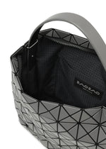 A close-up of the VALLEY tote by BAO BAO ISSEY MIYAKE shows its open geometric gray design with black triangles, gusseted sides, fabric-lined interior, inside pocket, and a “BAO BAO ISSEY MIYAKE” label.