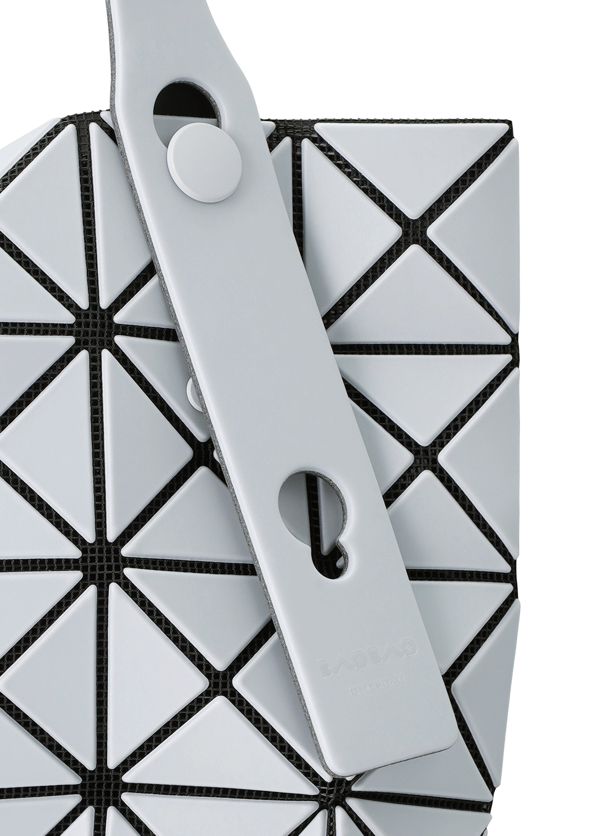 Zoomed view Close-up of a PRISM FROST tote bag by BAO BAO ISSEY MIYAKE, showing geometric light gray panels with black mesh, matte fabric-grain texture, and two overlapping straps with round cutouts and a snap button.