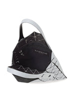 The PRISM FROST tote by BAO BAO ISSEY MIYAKE features a geometric white and black design, matte flexible triangular panels, a black interior, and an inner zip pocket labeled BAO BAO. The bag is partially open to show its details.