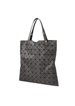 The PRISM DENIM by BAO BAO ISSEY MIYAKE is a black tote bag crafted from durable denim with a geometric triangular pattern, two handles, and a secure zippered interior pocket, shown against a white background.