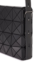 Close-up of OBLONG by BAO BAO ISSEY MIYAKE, a black minimalist handbag with a geometric triangular pattern, wide strap with metal buckles and adjustable holes, set against a clean white background.