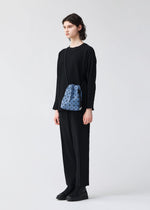 A person with short brown hair stands against a plain background, dressed in a loose black outfit and shoes, carrying the BAO BAO ISSEY MIYAKE WRING DENIM small blue crossbody bag with a geometric pattern.