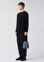 A person holds the BAO BAO ISSEY MIYAKE WRING DENIM, a small geometric-patterned blue and gray drawstring bag, while wearing black attire and standing against a plain light background.