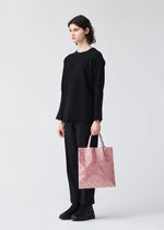 A person stands against a plain light background, dressed in all black and holding the BAO BAO ISSEY MIYAKE LUCENT METALLIC geometric pink tote bag in their left hand.