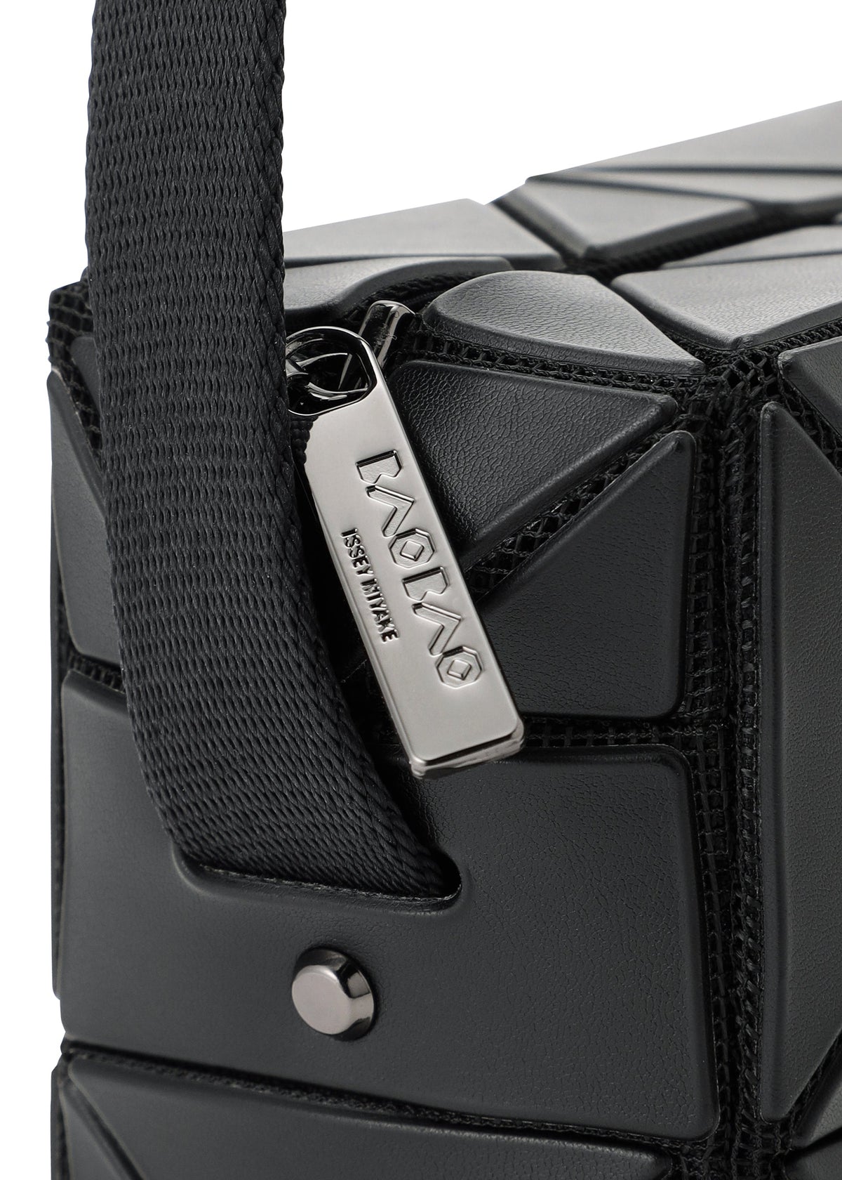 Close-up of the BAO BAO ISSEY MIYAKE CUBOID bag in black with a geometric texture, chunky adjustable strap, and a silver zipper pull engraved with the brand, set against the bag’s structured angular surface. view 5 of 8