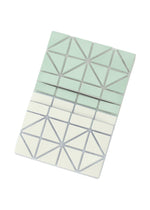 The CARD CASE W COLOR by BAO BAO ISSEY MIYAKE features a geometric two-tone design with light green and white triangles divided by metallic lines, shown against a white background.