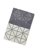 The CARD CASE W COLOR by BAO BAO ISSEY MIYAKE features a rectangular design with a two-tone geometric triangle pattern—dark gray on top, light gray on bottom—highlighted by visible stitched outlines.