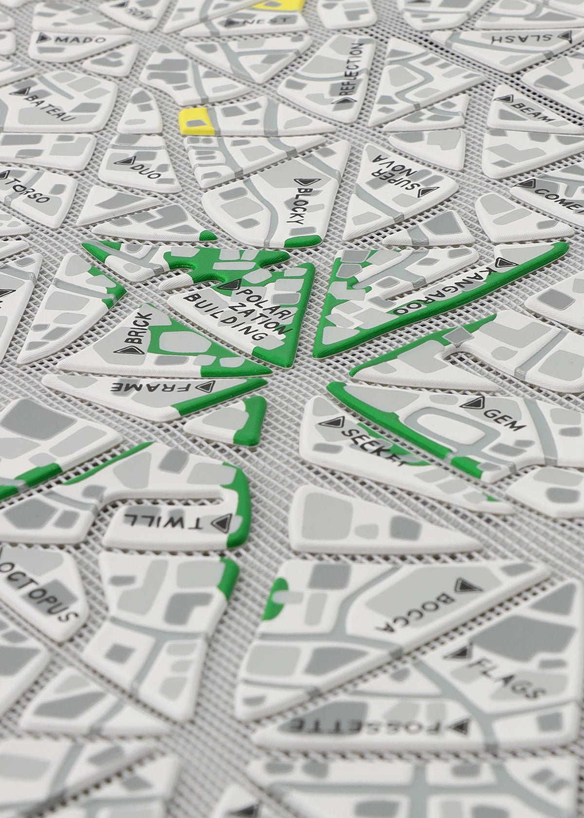 A close-up of MAP by BAO BAO ISSEY MIYAKE, a tactile city map with raised triangular sections, black street names, green route lines, and yellow-highlighted areas inspired by the brand's iconic design. view 7 of 10