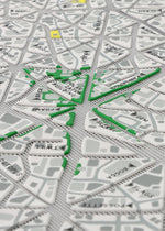 A close-up of MAP by BAO BAO ISSEY MIYAKE, a tactile city map with raised triangular sections, black street names, green route lines, and yellow-highlighted areas inspired by the brand's iconic design.