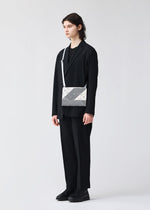 A person with long hair, dressed in a black suit, shirt, and shoes, stands before a white background holding the SIGN geometric silver shoulder bag by BAO BAO ISSEY MIYAKE, featuring a white strap.